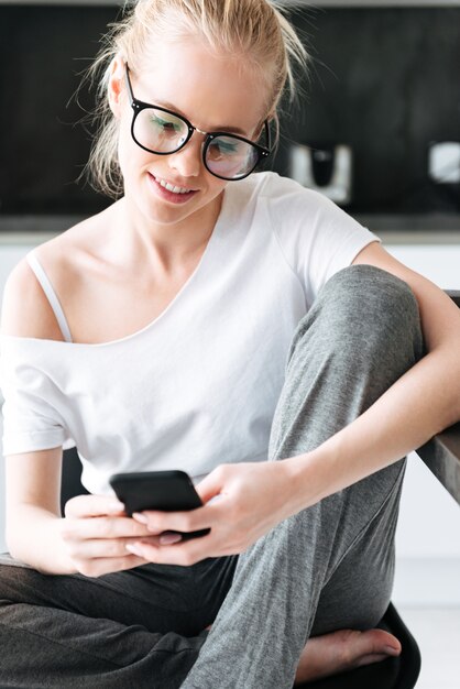 Retrato de joven enfocada con smartphone mientras está sentado en la cocina