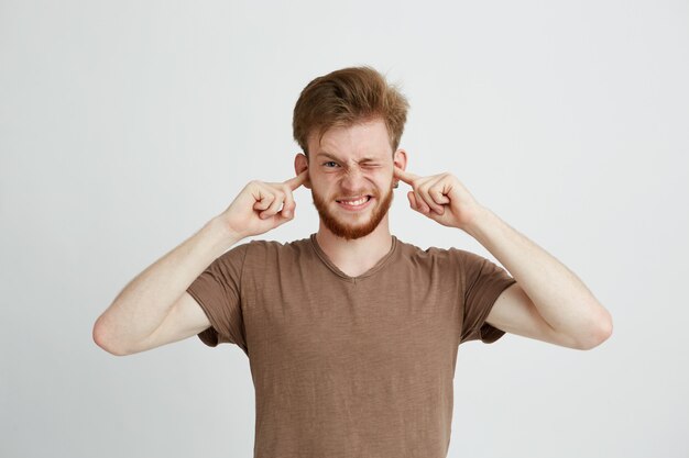 Retrato de joven enojado disgustado con barba cerrando los oídos.