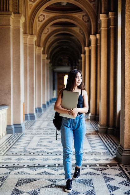 Retrato de joven estudiante asiática usando una computadora portátil o tableta en pose inteligente y feliz en la universidad o colegio,