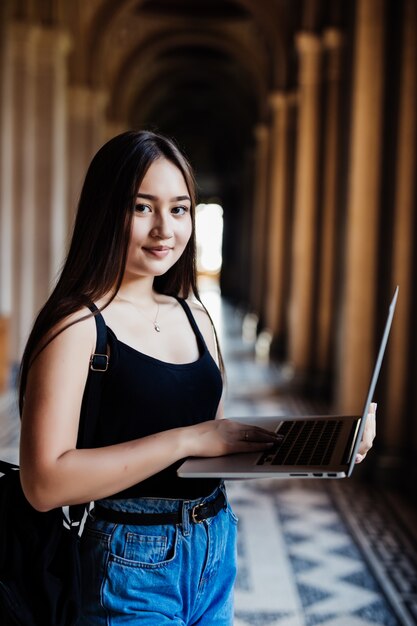 Retrato de joven estudiante asiática usando una computadora portátil o tableta en pose inteligente y feliz en la universidad o colegio,
