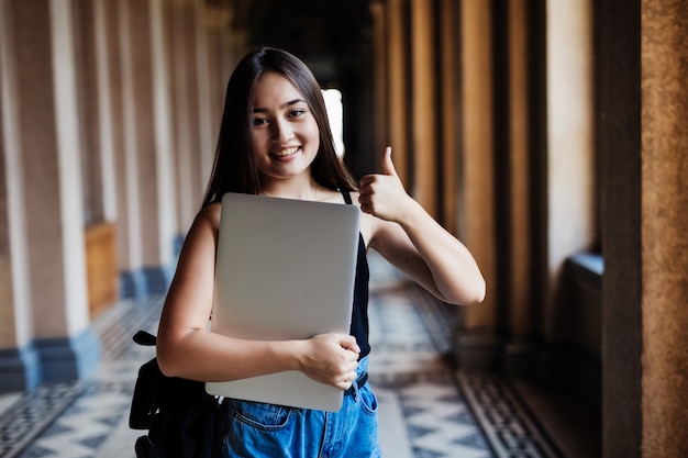 Retrato de joven estudiante asiática usando una computadora portátil o tableta en pose inteligente y feliz en la universidad o colegio,