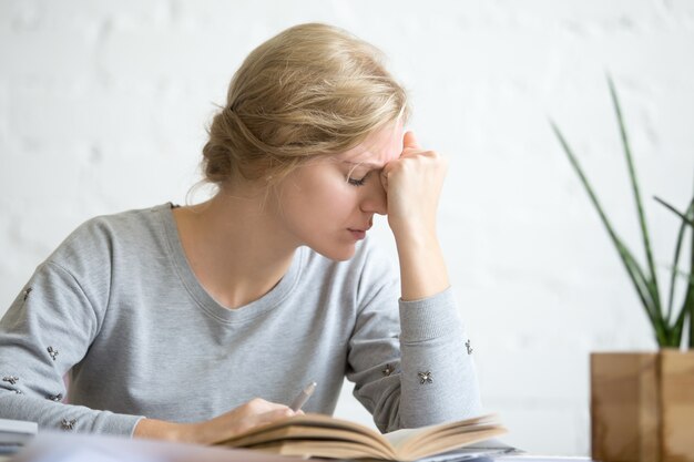 Retrato de una joven estudiante con exceso de trabajo sentado en la mesa