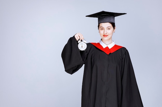 Retrato de joven estudiante graduada sosteniendo el reloj para mostrar el tiempo. Foto de alta calidad