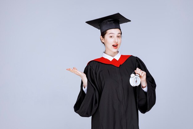 Retrato de joven estudiante graduada sosteniendo el reloj para mostrar el tiempo. Foto de alta calidad