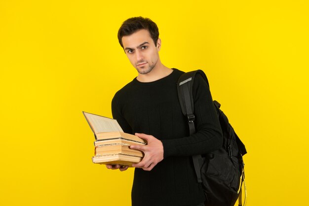 Retrato de joven estudiante leyendo libros sobre pared amarilla