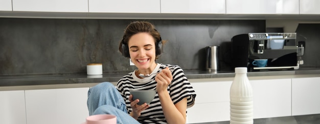 Foto gratuita retrato de una joven estudiante sonriente y sincera comiendo cereales matutinos y escuchando su desayuno