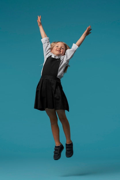 Foto gratuita retrato de una joven estudiante con uniforme escolar saltando en el aire