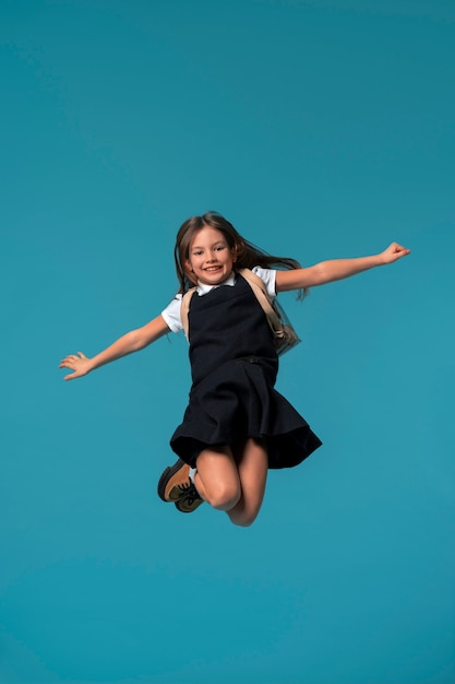 Foto gratuita retrato de una joven estudiante con uniforme escolar saltando en el aire