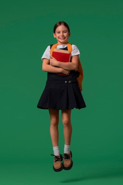 Retrato de una joven estudiante con uniforme escolar saltando en el aire