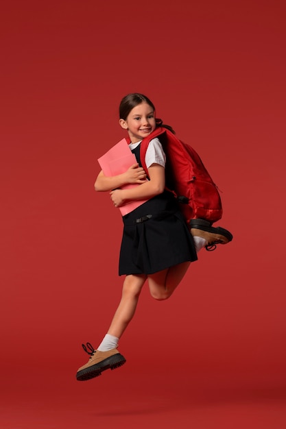 Retrato de una joven estudiante con uniforme escolar saltando en el aire