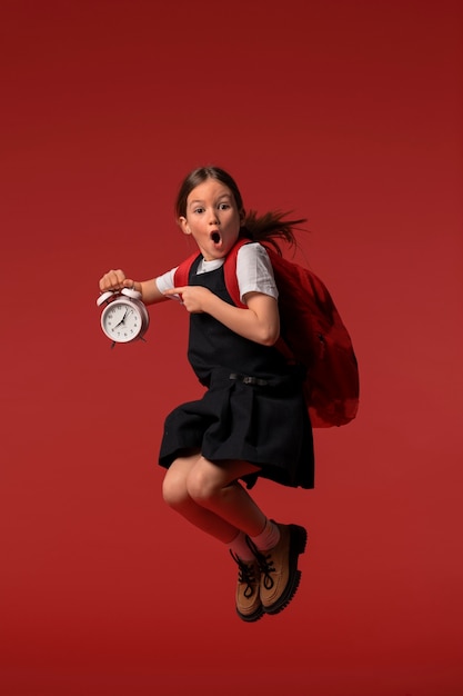 Retrato de una joven estudiante con uniforme escolar saltando en el aire