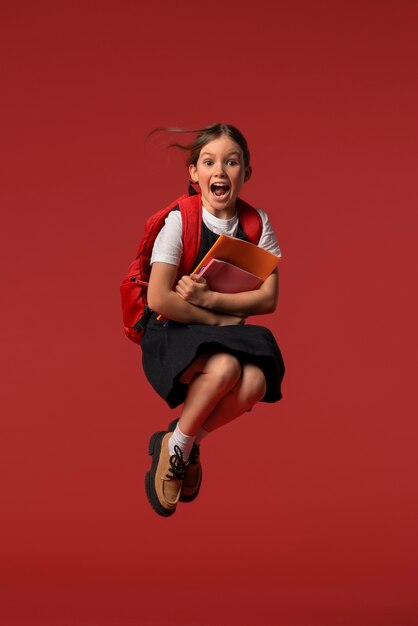 Retrato de una joven estudiante con uniforme escolar saltando en el aire