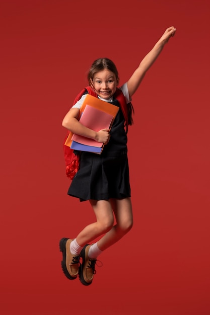 Retrato de una joven estudiante con uniforme escolar saltando en el aire