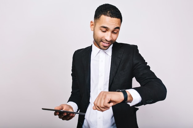 Retrato joven exitoso hombre ocupado en camisa blanca, chaqueta negra, con tableta mirando el reloj. Hombre de negocios elegante, ocupado, tiempo para trabajar, reuniones, liderazgo.