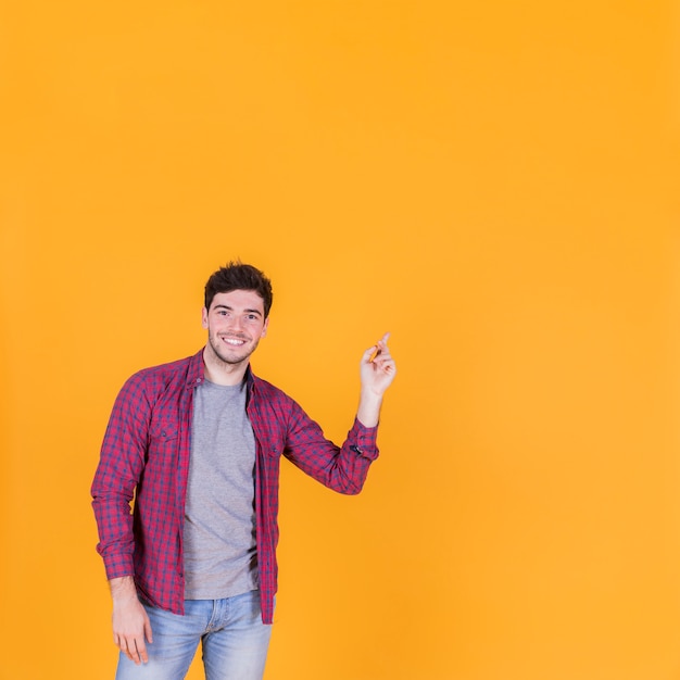 Retrato de un joven feliz apuntando su dedo contra un telón de fondo naranja