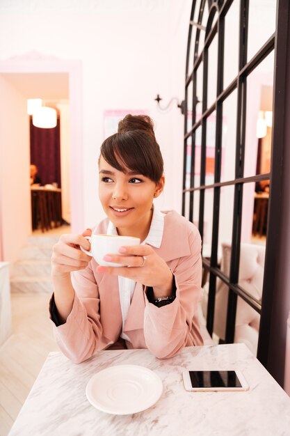 Retrato de una joven feliz en chaqueta rosa tomando café