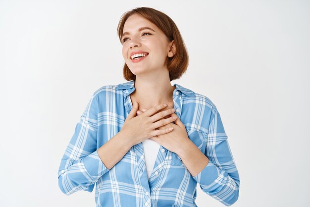 Retrato de una joven feliz cogidos de la mano en el corazón sonriendo agradecida decir gracias expresar gratitud y fascinación mirando a un lado el fondo blanco del espacio de la copia