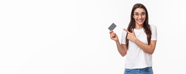 Foto gratuita retrato de una joven feliz y emocionada hablando de su banco apuntando a la tarjeta de crédito y a la cámara sonriente