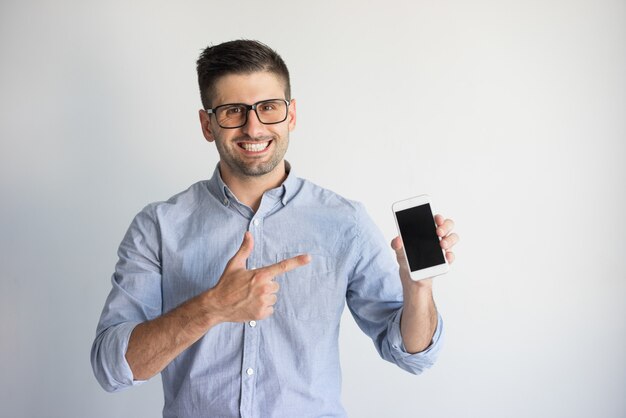 Retrato de joven feliz en gafas mostrando nuevo teléfono inteligente.