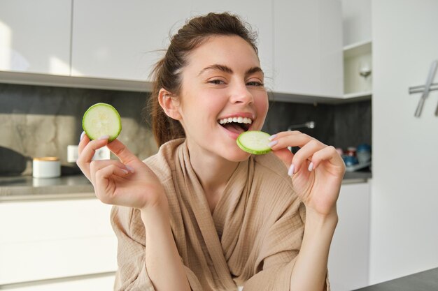 Foto gratuita retrato de una joven feliz y sonriente en la cocina cocinando picando calabacines sosteniendo verduras