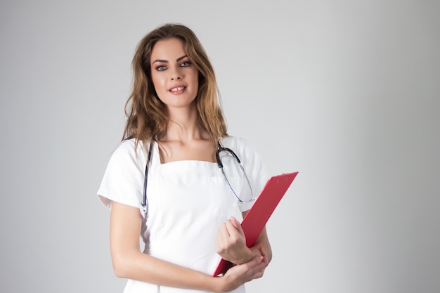 Retrato de joven feliz sonriente médico femenino sosteniendo un portapapeles de registro médico.