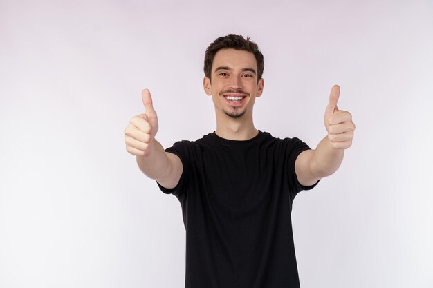 Retrato de un joven feliz y sonriente que muestra un gesto de pulgar hacia arriba y mira la cámara aislada sobre el fondo blanco