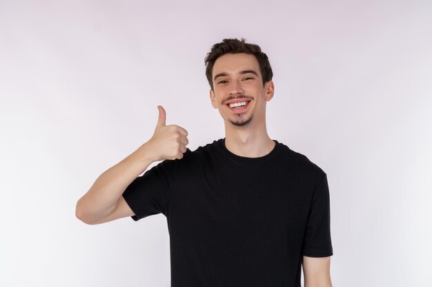 Retrato de un joven feliz y sonriente que muestra un gesto de pulgar hacia arriba y mira la cámara aislada sobre el fondo blanco