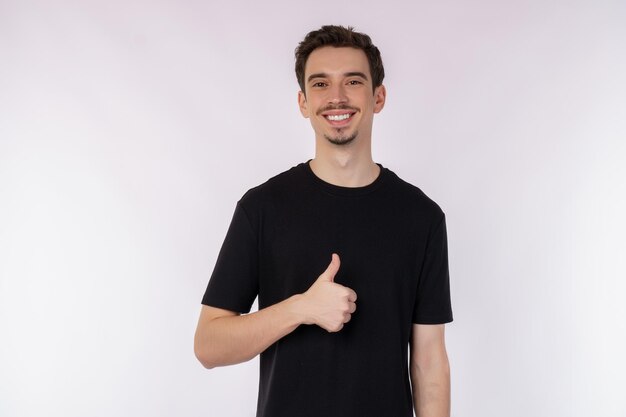 Retrato de un joven feliz y sonriente que muestra un gesto de pulgar hacia arriba y mira la cámara aislada sobre el fondo blanco