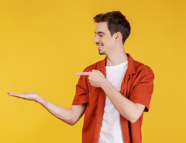 Retrato de un joven feliz y sonriente que presenta y muestra su texto o producto aislado en un fondo amarillo