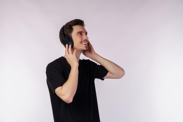 Retrato de un joven feliz usando auriculares y disfrutando de la música sobre fondo blanco.