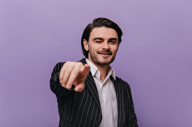 Retrato de joven feliz vestido con camisa blanca, traje negro mirando directamente mientras apunta a la cámara