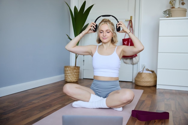 Foto gratuita retrato de una joven de fitness, una mujer que se entrena en casa y escucha a un instructor de fitness en línea inalámbrica