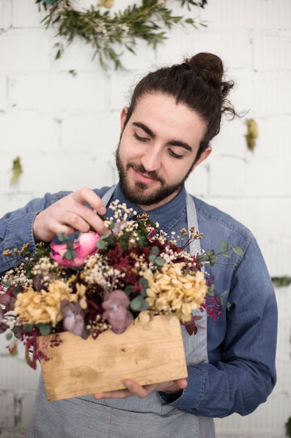 Retrato de un joven florista masculino sonriente arreglando las flores en la caja de madera