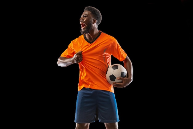 Retrato de joven futbolista africano posando aislado sobre fondo negro Concepto de deporte