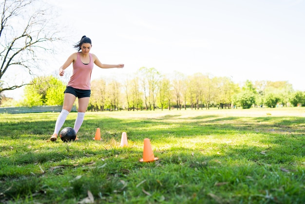 Retrato de joven futbolista corriendo alrededor de conos mientras practica con la pelota en el campo