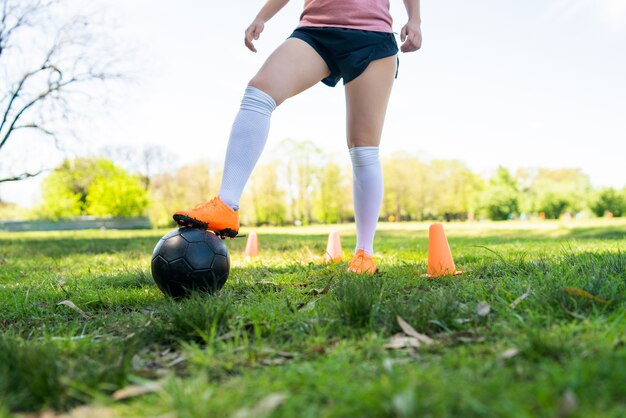 Retrato de joven futbolista corriendo alrededor de conos mientras practica con la pelota en el campo