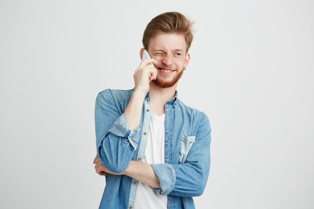 Retrato de joven guapo con barba sonriendo hablando por teléfono.