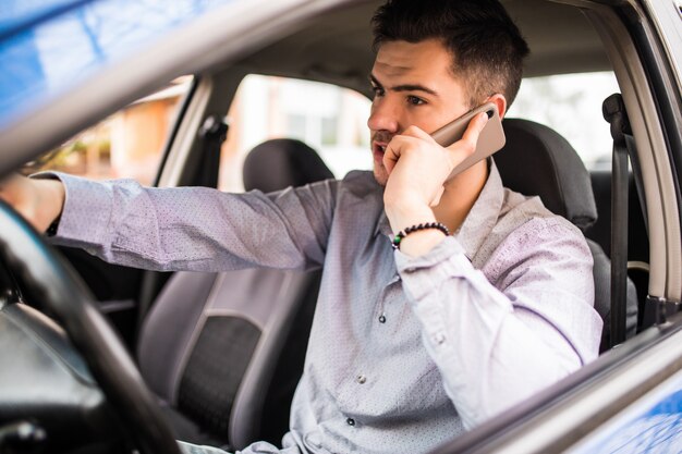 Retrato de joven guapo conduciendo y hablando por teléfono móvil.