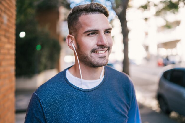 Retrato de joven guapo escuchando música con auriculares al aire libre en la calle. Concepto urbano.