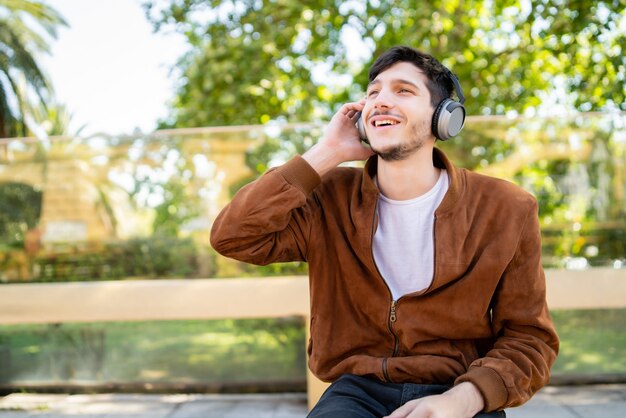 Retrato de joven guapo escuchando música con auriculares mientras está sentado al aire libre. Concepto urbano.