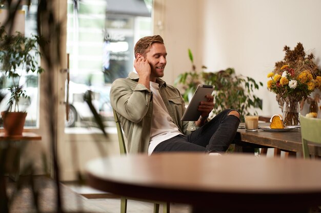 Retrato de un joven guapo y feliz sentado en un café viendo videos en una tableta digital