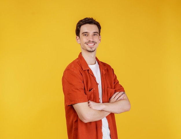 retrato, de, joven, guapo, hombre estar de pie, con, brazos cruzados, con, aislado, en, estudio, fondo amarillo