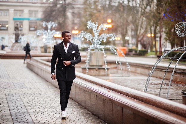 Retrato de joven y guapo hombre de negocios afroamericano en traje caminando en el centro de la ciudad con guirnaldas