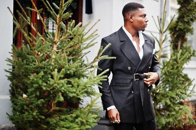 Retrato de joven y guapo hombre de negocios afroamericano en traje cerca de las decoraciones del árbol de año nuevo