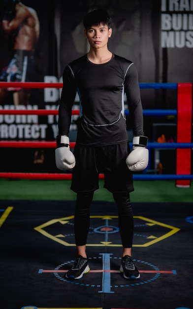 Retrato joven guapo en ropa deportiva y guantes de boxeo blancos pose de pie sobre lienzo en el gimnasio, clase de boxeo de entrenamiento de hombre sano,