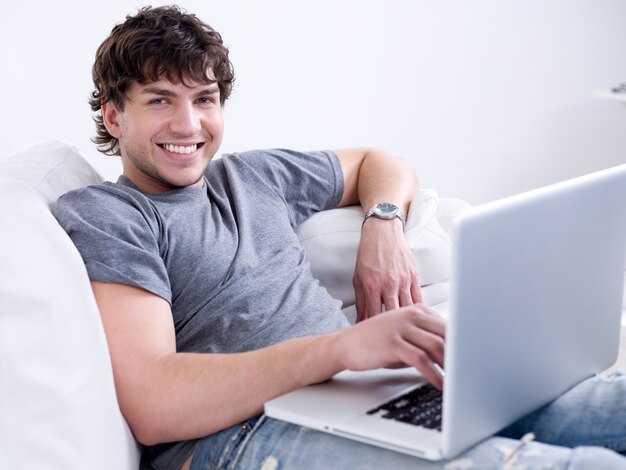 Retrato de joven guapo sonriente trabajando en el portátil en casa