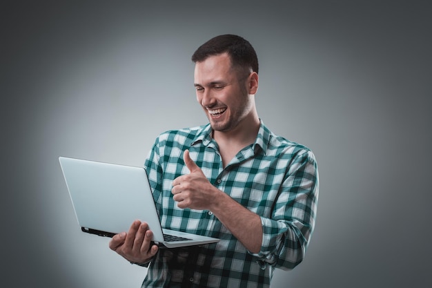 Foto gratuita retrato de un joven guapo usando una computadora portátil, con una camisa a cuadros. fotografía de estudio. emociones