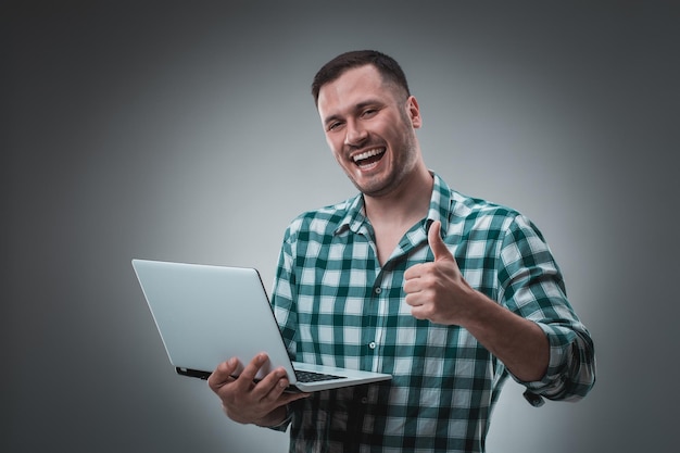 Retrato de un joven guapo usando una computadora portátil, con una camisa a cuadros. Fotografía de estudio. Emociones