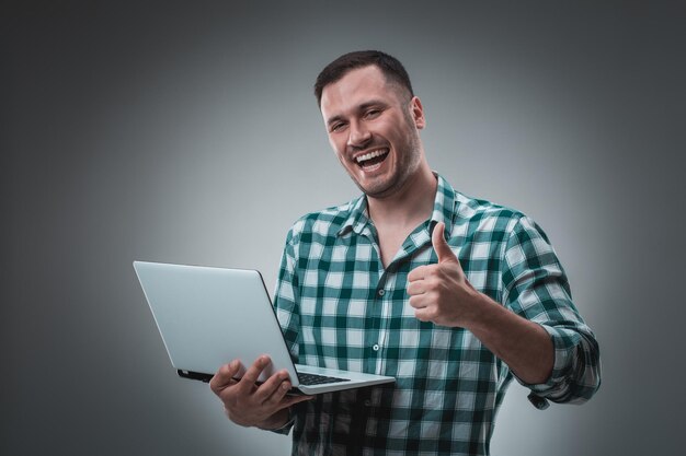 Retrato de un joven guapo usando una computadora portátil, con una camisa a cuadros. Fotografía de estudio. Emociones