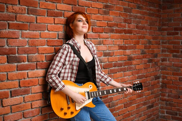 Retrato de joven con guitarra sobre fondo de ladrillo.